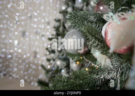 Albero di Natale decorato con giocattoli di colore argento e rosa. In esso vediamo i palloncini con nastri e luci che illuminano garland. Foto Stock