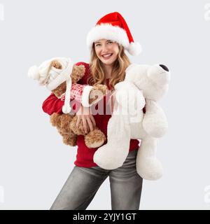 Buon Natale, la giovane donna felice e gioiosa che indossa un cappello di Babbo Natale sorride mentre tiene con grande tenerezza gli orsacchiotti, abbracciandoli saldamente Foto Stock