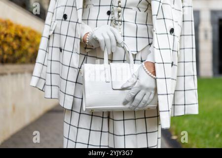 Donna alla moda all'aperto in città vestita con elegante tuta a scacchi con Blazer e pantaloni, borsa bianca, dettagli in mostra abbigliamento alla moda e St Foto Stock