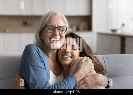 Felice donna anziana in occhiali che coccola strettamente la sua figlia adulta Foto Stock