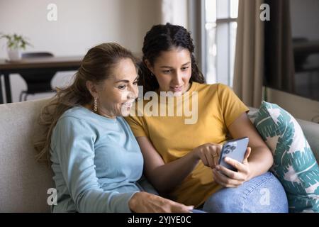 Figlia latina che insegna a madre anziana a utilizzare l'applicazione per la casa intelligente Foto Stock