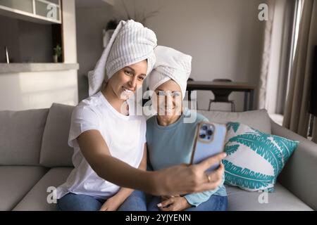 Figlia felice e mamma matura in teli per la testa che si fanno selfie Foto Stock