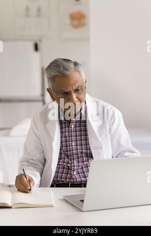 Un medico serio seduto alla scrivania prende appunti sulla rivista medica Foto Stock