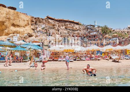 Sharm El Sheikh, Egitto - 5 maggio 2024: Spiaggia affollata di Farsha con ombrelloni colorati, acque turchesi cristalline e scogliere adornano Foto Stock