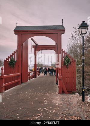Durante il mercatino di Natale, i visitatori attraversano un ponte di legno rosso decorato nella fortezza di Bourtange, creando un'atmosfera festosa. Foto Stock