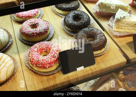 Torte di ciambelle in glassa di cioccolato rosa con spruzzi colorati nella finestra del caffè. Vendita di dolci tradizionali. Foto Stock