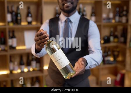 Primo piano medio di un'esclusiva bottiglia di vino nelle mani dell'irriconoscibile sommelier afroamericano che la dimostra Foto Stock