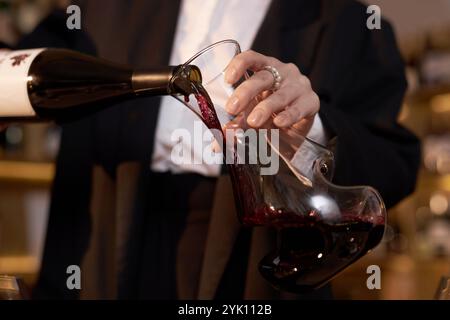 Il primo piano di una mano femminile elegante e irriconoscibile di sommelier che versa vino rosso in una caraffa di vetro di cristallo per aprire il bouquet Foto Stock