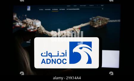 In questa immagine, una persona ha in mano un cellulare con il logo dell'azienda petrolifera Abu Dhabi National Oil Company (ADNOC) davanti alla pagina Web aziendale. Foto Stock