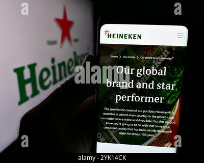 In questa illustrazione fotografica, una persona ha un telefono cellulare con il sito web della birreria olandese Heineken NV davanti al logo aziendale. Foto Stock