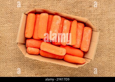 Piccola carota sbucciata con piastra di carta su panno di iuta, macro, vista dall'alto. Foto Stock