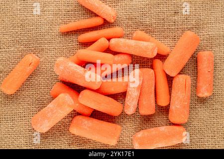 Piccola carota sbucciata su un panno di iuta, macro, vista dall'alto. Foto Stock