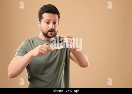 Uomo emotivo che prende i capelli persi dal pettine su sfondo beige, spazio per il testo. Problema di alopecia Foto Stock