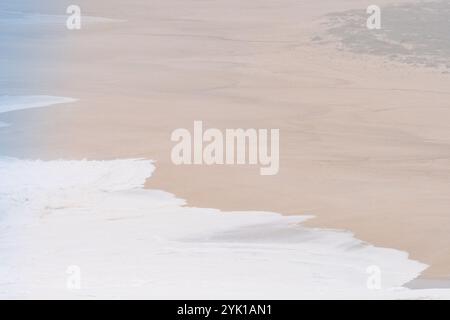 Morbide onde bianche che si infrangono dolcemente su una vasta spiaggia di sabbia a Nazare, in Portogallo Foto Stock