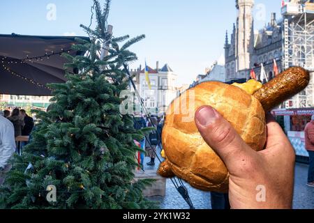 16 novembre 2024: Bratwurst in un roll con senape in un mercatino di Natale, sullo sfondo un albero di Natale e visitatori del mercatino di Natale decorati a festa. FOTOMONTAGGIO *** Bratwurst im Brötchen mit Senf auf einem Weihnachtsmarkt, im Hintergrund ein festlich geschmückter Tannenbaum und Weihnachtsmarkt-Besucher. FOTOMONTAGE Foto Stock