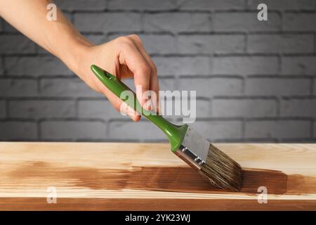 Donna con spazzola che applica macchia di legno di noce su una superficie di legno, primo piano Foto Stock