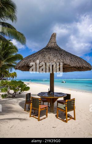 Tavolo e sedie con ombrellone in paglia sulla spiaggia al Paradis Beachcomber Golf Resort Foto Stock