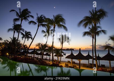 Riflesso di palme da cocco e ombrelli di paglia nella piscina del Royal Palms Beachcomber Luxury (Beachcomber Resorts) al tramonto, Grand Baie, R. Foto Stock