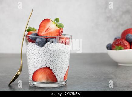 Budino di Chia con bacche: Fragole, mirtilli e latte di cocco su sfondo grigio. Concetto di cibo sano. Copia spazio. Foto Stock