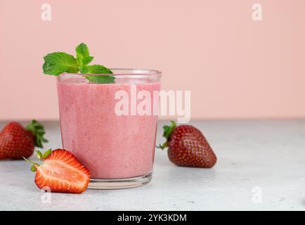 Frullato di fragole o frullato di latte con frutti di bosco su sfondo rosa. Bevande estive. Copia spazio. Foto Stock