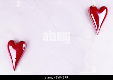 Un paio di mani reggono delicatamente cuori di porcellana rossa su uno sfondo di marmo bianco, celebrando l'amore e San Valentino in una vista dettagliata dall'alto verso il basso Foto Stock