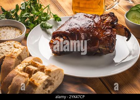 Noci di maiale al forno su un piatto bianco su uno sfondo di legno o un tavolo con pane, cetrioli freschi, prezzemolo e senape. Piatto tradizionale bavarese. Alto Foto Stock