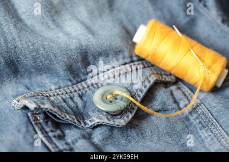 Bottoni, filetto e ago per cucire su denim. Fatto a mano. Primo piano Foto Stock