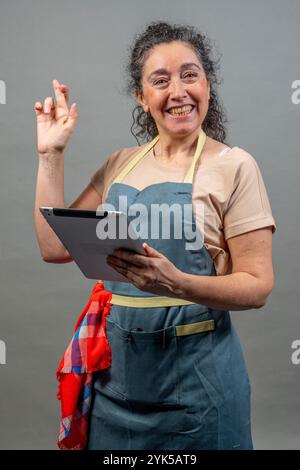 Chef felice con un tablet che esprime un desiderio con le dita incrociate, sperando in un successo nel business online Foto Stock