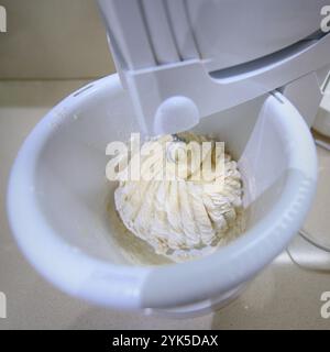 Utilizzare un mixer elettrico per montare l'impasto per torte in un recipiente bianco su un ripiano della cucina. Foto Stock