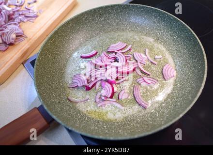 Le cipolle rosse a fette vengono saltate in una padella con olio, creando un delizioso aroma in cucina. Foto Stock