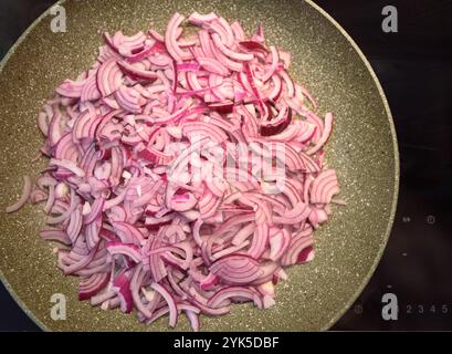 Le cipolle rosse a fette stanno cucinando in una padella a fuoco medio, rilasciando il loro aroma saporito mentre vengono preparate per un piatto. Foto Stock