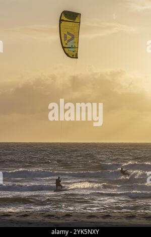 Due kitesurfer che scivolano sul mare al tramonto, atmosfera suggestiva con toni gialli e arancioni, kitesurfer alla luce della sera, Texel Foto Stock