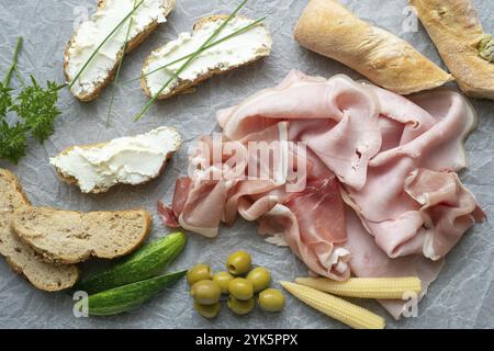 Antipasto freddo. Salumi. Spuntini diversi su carta bianca, prosciutto, pane, verdure, dall'alto Foto Stock