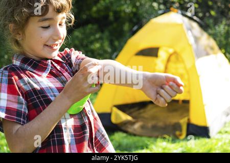 Ragazza spruzza zanzara spray sulla pelle in natura che mordono le mani e i piedi. Protezione da punture di insetti, repellente sicuro per i bambini. Recr. Esterno Foto Stock