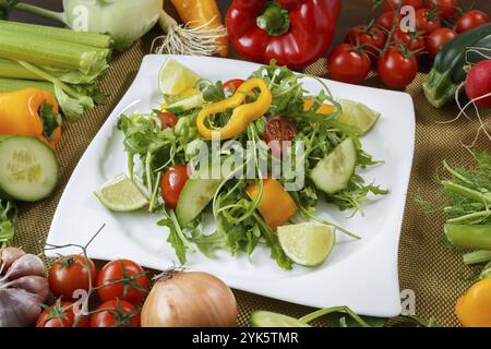 Un ambiente di alimentazione sano. Verdure e insalata diverse con verdure a foglia e pomodori ciliegini su piatto bianco Foto Stock