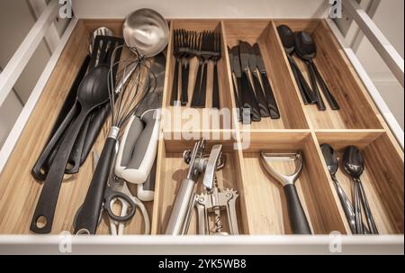 Un cassetto della cucina ordinato presenta un assortimento di utensili da cucina, tra cui fruste e posate, ordinatamente organizzati in sezioni separate per la massima comodità. Foto Stock