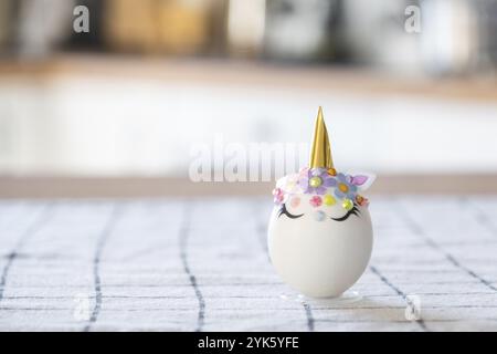 Artigianato pasquale, decora un uovo a forma di unicorno con strass, corno, fiori all'interno di una casa Foto Stock