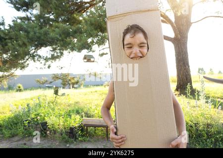 Il bambino è divertente ballare e ingannare in un costume da scatola, ritaglio rotondo per viso e mani. Trasferirsi in una nuova casa, giochi per bambini da improvvisazioni Foto Stock