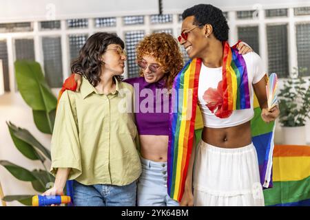 Amici lgbt multietnici che cantano karaoke e festeggiano con bandiere arcobaleno a casa Foto Stock