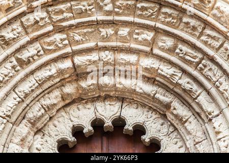 Un arco in pietra splendidamente intagliato incornicia le grandi porte in legno di un'antica chiesa di Obanos, che mostra intricata maestria artigianale. Foto Stock