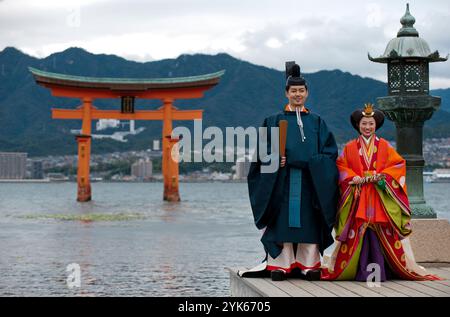 Una coppia di nozze in tradizionale abito del periodo Heian posa per una foto al Santuario di Itsukushima sull'isola di Miyajima, prefettura di Hiroshima, Giappone. Foto Stock