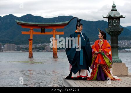 Una coppia di nozze in tradizionale abito del periodo Heian posa per una foto al Santuario di Itsukushima sull'isola di Miyajima, prefettura di Hiroshima, Giappone. Foto Stock