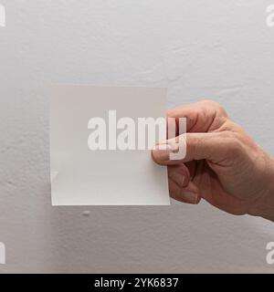 Mano con un foglio bianco vuoto su uno sfondo normale, ideale per i messaggi Foto Stock