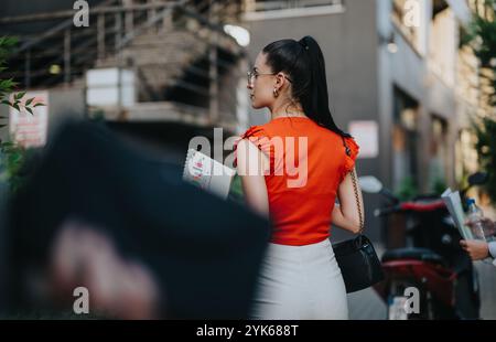 Donna d'affari in cima rossa che tiene documenti sulla strada della città Foto Stock