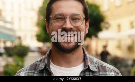 Uomo sorridente felice barbuto uomo d'affari caucasico turista cliente viaggiatore in occhiali da vista allegro guardando la macchina fotografica città città città strada amichevole Foto Stock
