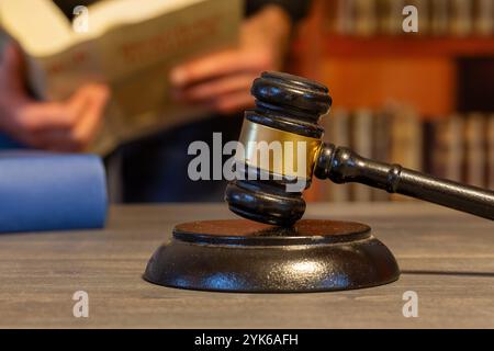 Primo piano di un martelletto di un giudice, sullo sfondo un uomo legge un libro di legge (immagine simbolo) Foto Stock