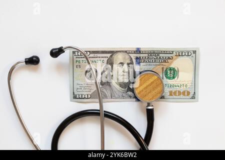 Lo stetoscopio del medico e la banconota da cento dollari si trovano su sfondo bianco, finanza e cura, medicina Foto Stock