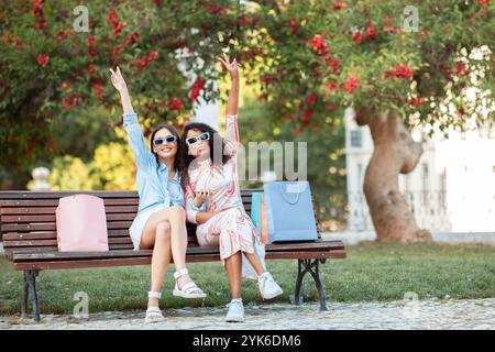 Due amici che si godono una giornata di sole nel parco con le borse dello shopping Foto Stock