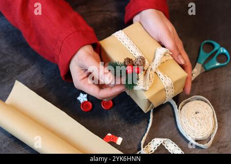 Mani di una ragazza in un abito rosso che decora una confezione regalo con nastro in pizzo. Mani femminili che tengono in mano una confezione regalo. Foto Stock