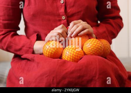 Donna in abito rosso con arance in borsa mesh su sfondo chiaro, primo piano delle mani Foto Stock